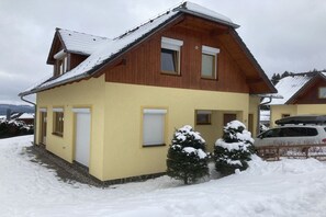 Ein zweistöckiges Holzhaus mit geneigtem Dach, einer Garage und einer verschneiten Landschaft.
