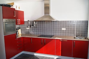 A kitchen with red cabinets, a stainless steel range hood, and a tiled backsplash. - Holiday home with 2 bedrooms (Lipno nad Vltavou)