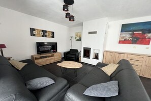 Ein modernes Wohnzimmer mit einem schwarzen Ledersofa, einem Holztisch, einem Flachbildfernseher und einem Kamin.