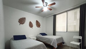 A room with two beds, a ceiling fan, a window with curtains, and a white chair. - Acogedor y cómodo, gym, alberca seguridad 24 horas (Zapopan)