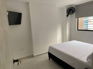 A bedroom with a bed, a television mounted on the wall, a standing fan, and a window with a view of buildings. - Aves María 6th floor with balcony and parking (Sabaneta)