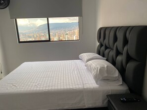 A hotel room with a bed, a window with a cityscape view, and a dark headboard. - Aves María 6th floor with balcony and parking (Sabaneta)