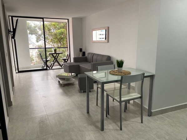 Un soggiorno moderno con tavolo da pranzo in vetro, divano grigio e una grande porta scorrevole in vetro che dà su un balcone.