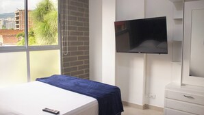 A hotel room with a bed, a TV mounted on the wall, and a window with a view of buildings and trees. - 41 September Promo in The Coolest Neighborhood (Medellín)