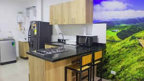 A kitchen with wooden cabinets, a gas stove, a refrigerator, and a microwave. - 41 September Promo in The Coolest Neighborhood (Medellín)