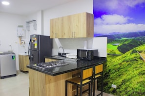 Una cocina con armarios de madera, estufa a gas, refrigerador y microondas.