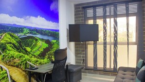 A room with a desk, office chair, and sofa. There's a TV mounted on the wall and a window with blinds. - 41 September Promo in The Coolest Neighborhood (Medellín)