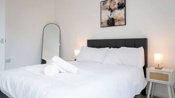 A hotel room with a bed, a bedside table with a lamp, a wall-mounted mirror, and a painting.