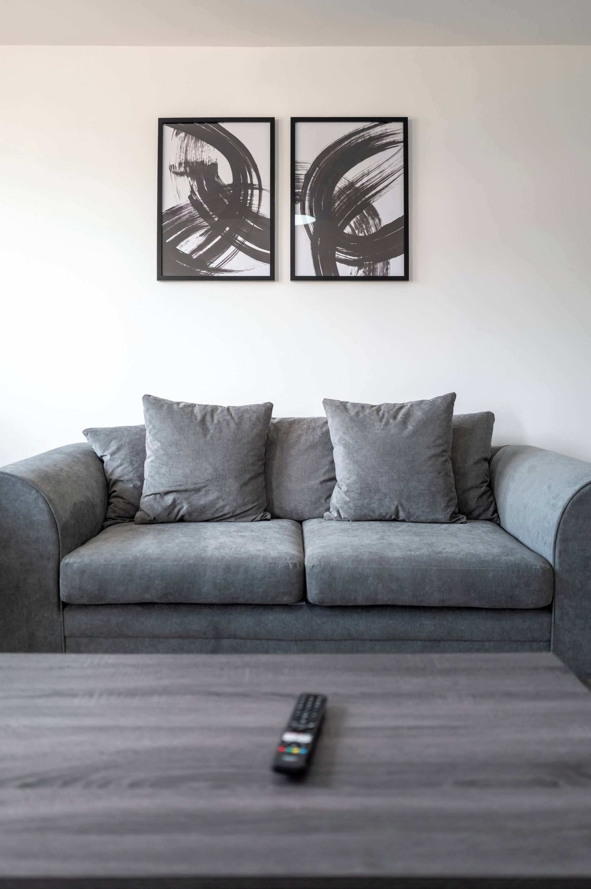 A grey sofa with two cushions and a remote control on a coffee table.