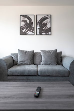 A grey sofa with two cushions and a remote control on a coffee table. - Modern 3BD Flat Hoxton & Shoreditch  N1 (Greater London)