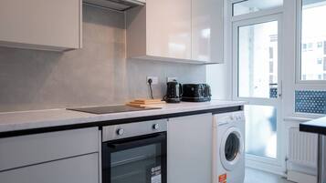 A modern kitchen with a built-in oven, a washing machine, and a coffee maker on the countertop.