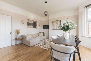 A modern living room with a sofa, a dining table with chairs, a TV, and artwork on the walls. - Stylish 3BED flat, great location (Greater London)