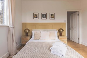 A bedroom with a bed, two bedside tables with lamps, a window with curtains, and three framed pictures on the wall. - Stylish 3BED flat, great location (Greater London)