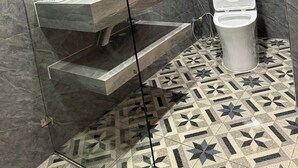 A bathroom with a marble wall, a glass-enclosed sink, a toilet, and patterned floor tiles. - La Armber Hotel (Luang Prabang)
