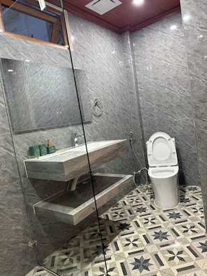 Ein Badezimmer mit Marmorwand, einem in Glas gefassten Waschbecken, einer Toilette und gefliestem Boden mit Muster.