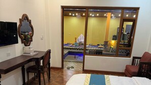 A hotel room with a bed, a desk, a chair, a television, and a window with a view of the pool area. - La Armber Hotel (Luang Prabang)