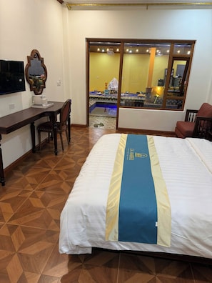 Ein Hotelzimmer mit Bett, Schreibtisch, Stuhl, Fernseher und einem Fenster mit Blick auf den Poolbereich.