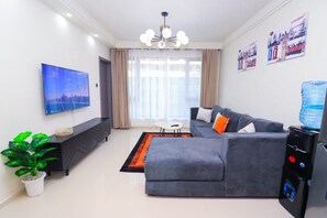 Ein modernes Wohnzimmer mit einem grauen Sofa, einem Flachbildfernseher, einer Topfpflanze und einem Wasserspender.