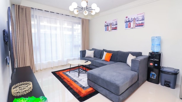 A modern living room with a grey sectional sofa, a small white table, a black coffee table, a water dispenser, and a trash bin. - Spacious 1-bedroom apartment in Westlands, Nairobi, Kenya (Nairobi)