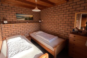 Ein Zimmer mit zwei Holzbetten, einer Ziegelwand, einem Gemälde, einer Holzkommode und einer Pendelleuchte.