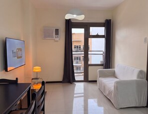A modern living room with a flat-screen TV, a small table with a lamp, a sofa, and a sliding glass door leading to an outdoor balcony. - Premier Double Room with Balcony and Manila Bay View, Pool View or MOA View (Pasay City)