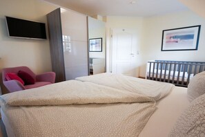 A hotel room with a bed, a TV mounted on the wall, a door, and a crib. - Holiday home in Zingst with swimming pool (Zingst)