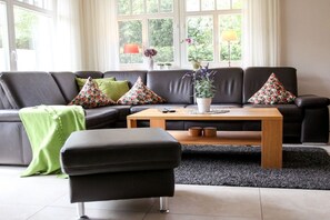 A modern living room with a sectional sofa, a coffee table, and a small ottoman. - Holiday home in Zingst with swimming pool (Zingst)