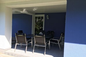 Een terras buiten met een tafel, stoelen, een raam en een wandlamp.