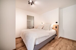 Ein Schlafzimmer mit einem Bett, Holzboden, einer Tür und einer Lampenleuchte.