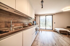 A modern kitchen with a wooden countertop, a built-in sink, and a large window offering a view of trees. - Houchma – Charming 4-Guest | Mt Blanc View | Spa | Lifts 400m (Les Houches)