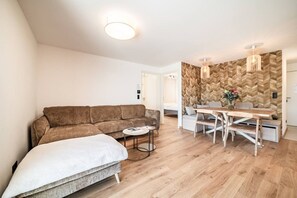 Ein modernes Wohnzimmer mit einem braunen Sofa, einem weißen Sessel, einem kleinen runden Tisch und einem Essbereich mit einem Holztisch und Bänken.