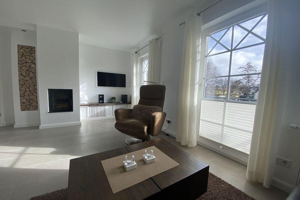 A modern living room with a brown leather chair, a flat-screen TV, and a large window with curtains.