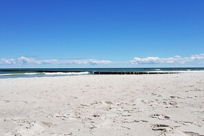 Ein Strand mit blauem Himmel, Wellen, die auf das Ufer zulaufen, und einem hölzernen Steg.