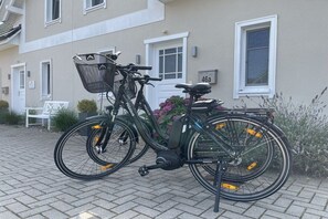 Ein stehendes Fahrrad mit Korb und Sitz, angelehnt an eine befestigte Fläche vor einem Gebäude mit einer Hausnummer.