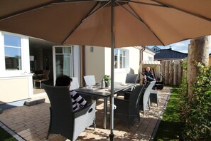 Eine Terrasse im Freien mit Tisch und Stühlen, einem großen Sonnenschirm und einem Holzzaun.
