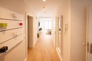 A hallway with a wooden floor, white walls, and a door leading to a room with a bed and a window. - Holiday apartment with 2 bedrooms (Zingst)