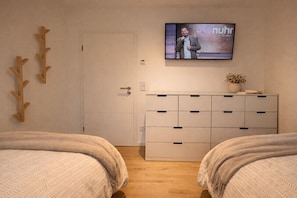 A bedroom with two beds, a TV on the wall, a white dresser, and a door. - Holiday apartment with 2 bedrooms (Zingst)