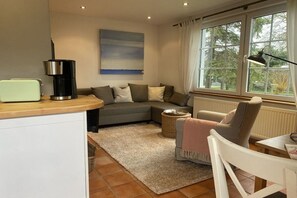 A cozy living room with a sofa, a coffee maker, a lamp, and a view of trees through the window. - "Under thatched roof" with view of the Bodden lagoon and sauna (Barth)
