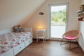 Un dormitorio con cama, mesita de noche, una silla y una ventana.