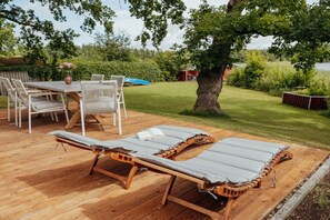 A wooden deck with lounge chairs and a table, surrounded by a grassy area and trees. - Lakefront property, bathing bay (Krakow am See)