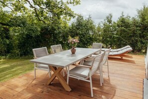 Una terraza al aire libre con una mesa y sillas, rodeada de follaje.