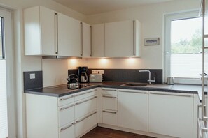 A compact kitchen with white cabinets, a black countertop, a kettle, a coffee maker, and a toaster. - Lakefront property, bathing bay (Krakow am See)