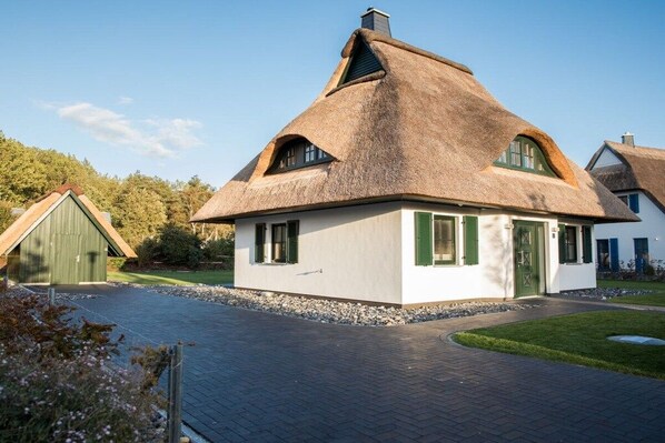 Ein Haus mit einem Strohdach, weißen Wänden und grünen Fensterläden.