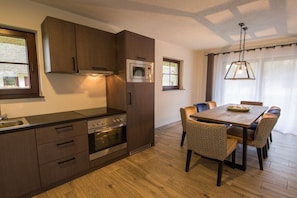 Eine moderne Küche mit dunklen Holzschränken, Edelstahlgeräten und einem Essbereich mit Holztisch und gemusterten Stühlen.