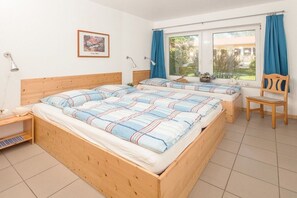 A room with two wooden beds, a chair, a desk, a lamp, and a window with curtains. - on the Baltic Sea - 1 bedroom (Rerik)