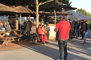 An outdoor seating area with wooden tables and benches, a covered structure, and a group of people. - Holiday apartment with 1 bedroom (Ostseeheilbad Zingst)