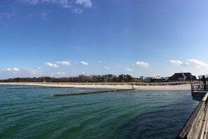 A coastal scene with a wooden pier extending into calm waters, a sandy beach, and buildings in the background. - Holiday apartment with 1 bedroom (Ostseeheilbad Zingst)