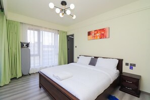 Ein Hotelzimmer mit einem großen Bett, einem Nachttisch, einem an der Wand befestigten Fernseher und einem Fenster mit Vorhängen.