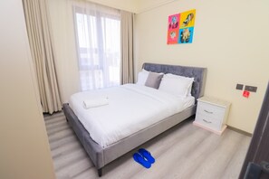 Ein Hotelzimmer mit einem Bett, einem Nachttisch, einem Fenster mit Vorhängen und einer Wand mit farbenfroher Kunst.