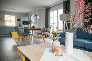 A modern living room with a wooden coffee table, a vase with flowers, and a glass candle holder. - Holiday home with 2 bedrooms (Fuhlendorf)